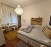 A bedroom in a two-room apartment with a wooden decor floor and minimalist furnishings.