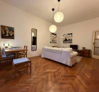 Living room in a two-room apartment with a wooden decor floor, a white sofa, and a table.