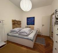 Bedroom in a two-room apartment with wood-patterned flooring, a bed, and a white cabinet.