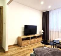 Living room in a 3-room apartment with a wooden decor floor and a large television.