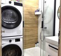 A bathroom in a 3-room apartment with a wooden decor floor, a shower corner, and a washing machine.