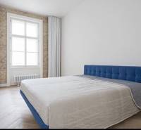 A bright bedroom in a 4-room apartment with a blue bed, a brick wall, and a wooden decor floor.