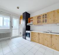 A kitchen with light tiles, wooden cabinets, and white appliances in a 4-room apartment.