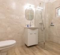 A bathroom with a wooden decor floor, a shower, and a cabinet in a 3-room apartment.