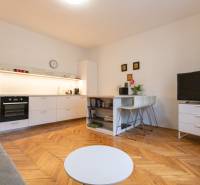 Living room in a two-room apartment with a kitchen, wooden decor flooring, TV, and table.