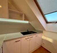A kitchen unit in a 2-room apartment with white cabinets and a large skylight.