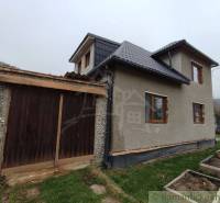 A family house in Jasenica with a wooden garage and garden planters on the lawn.