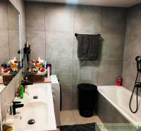 A bathroom in a family house with a bathtub, double sink, and light gray wall tiles.