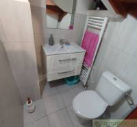 Bathroom in a family house with a sink, mirror, and toilet on light tiles.
