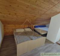 Attic bedroom in a family house with two beds and a wooden decor floor.