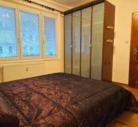 A bedroom with a large wardrobe and a bed with a dark quilted bedspread, wooden decor flooring.