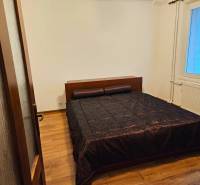 A bedroom in a 3-room apartment with a wooden decor floor and a dark bedspread.