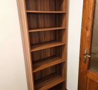 A shelf with five shelves next to wooden doors and a floor with a wooden decor.