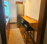 A narrow kitchen in a 3-room apartment with a gas stove, refrigerator, and a wooden decor floor.