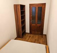 A room in a 3-room apartment with a wooden decor floor, a bed, and a bookshelf.