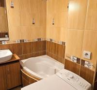 A bathroom with a corner bathtub, a washing machine, and a sink in a 3-room apartment.