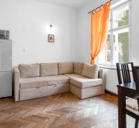 Living room in a two-room apartment with a wooden decor floor, a sofa, and orange curtains.