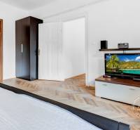 Bedroom in a 2-room apartment with wood-patterned flooring, wardrobes, and a television.