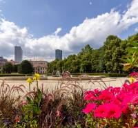A garden with flowers and a fountain, with high-rise buildings in the background in Bratislava - Old Town.