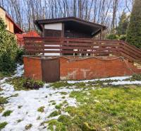 A cottage in Šemša surrounded by greenery and snow, with a terrace and a brick foundation.