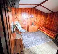 A room in a cabin with wooden paneling, an armchair, a bench, a carpet, and a bed.