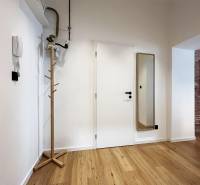 A hallway with a coat rack and a mirror, white walls, wooden floor, in a 2-room apartment on Vajnorská.