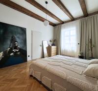 A bright bedroom with wooden ceiling beams, a painting on the wall, and subtle decoration.