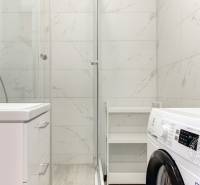 A bathroom with white tiles, a shower corner, and a washing machine in a 3-room apartment.