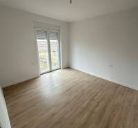 An empty room in a 3-room apartment with a wood-patterned floor and a French window.