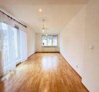 A bright living room in a two-room apartment with wood-patterned flooring and large windows.