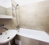 Bathroom in a 2-room apartment with a bathtub, sink, and light ceramic tiles.