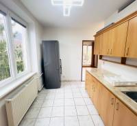 A kitchen in a 2-room apartment with windows, tiles, and wooden decor cabinets.