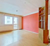 Living room with light walls, orange accent, and wood-patterned flooring in a three-room apartment.