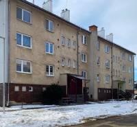 A three-story apartment building on Družstevná Street in Podolínec with a snow-covered lawn.