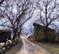 Blatová cesta v Krásnohorskom Podhradí na Mierovej ulici, obklopená stromami a budovami. Pozemky - bývanie.