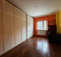 A room with an orange wall, a large wardrobe, and a wooden-patterned floor in a 3-room apartment.