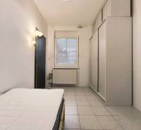 A room in a family house with a bed, a wardrobe, and a window, tiled floor.