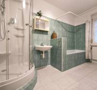 Bathroom in a family house with a bathtub, shower, sink, and tiled walls.
