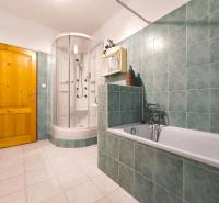 A bathroom in a family house with a bathtub, a shower corner, and green tiles.