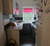A narrow kitchen with black and white cabinets and a large white refrigerator in a family house.