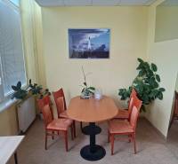 Office with an oval table and four chairs, plants, and a painting on the wall.