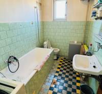 A bathroom in a family house with a bathtub and a window, with colorful tiles and green wall tiles.