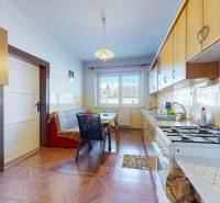 A kitchen with a wood-patterned floor, light-colored furniture, and a dining table in a family house.