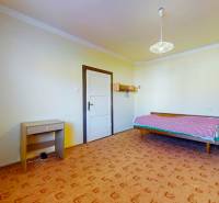 A room in a family house with a bed, a table, and a patterned carpet.