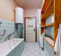 A bathroom in a family house with a bathtub, water heating, and a wooden shelf.