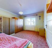 A bedroom with a bed, wardrobes, a window, and a cross in a family house.