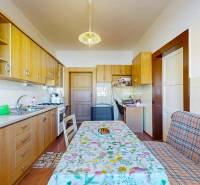 A kitchen in a family house with a wooden-patterned floor and a patterned tablecloth on the table.