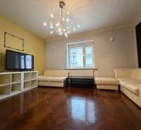 Living room with white sofas, wood-patterned flooring, and a light chandelier in a three-room apartment.