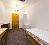 A room in a family house with a bed, wardrobe, and table, complemented by white lighting and carpeted flooring.