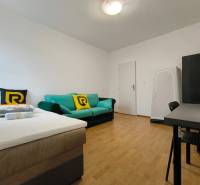 A room in a family house with a bed, a sofa, and a desk, with a wooden-decor floor.